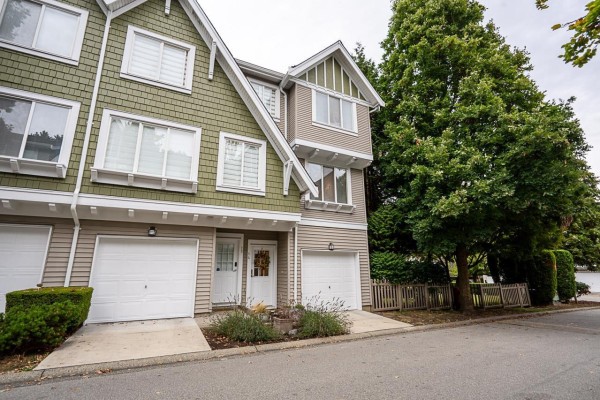 Close-up of multi-story townhouses with green and beige siding, showing garages and doors. - 14 8775 161 Street, Surrey