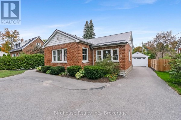 Side view of a red brick bungalow with a metal roof, driveway, and detached garage. - 14 Angeline Street S, Kawartha Lakes