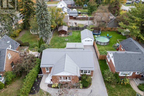 Aerial view of a red brick bungalow with a metal roof, backyard, swimming pool, and garage. - 14 Angeline Street S, Kawartha Lakes