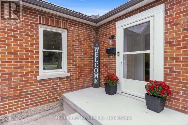 Close-up of the front door of a red brick bungalow with a window, mailbox, and potted plants. - 14 Angeline Street S, Kawartha Lakes