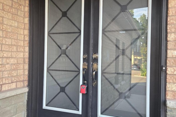 Close-up of a double front door with decorative glass panels and brass hardware, a red lockbox attached. - 14 Archibald Street, Brampton