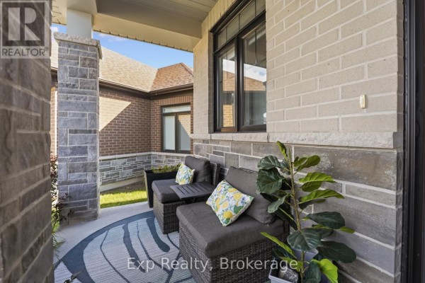 Covered front porch with grey wicker seating, a patterned rug, and potted plants. - 14 Athabaska Drive, Belleville