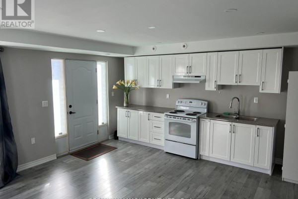 View of the kitchen and living area with grey flooring and white cabinets. - 14 #basement - 3029 Finch Avenue W, Toronto