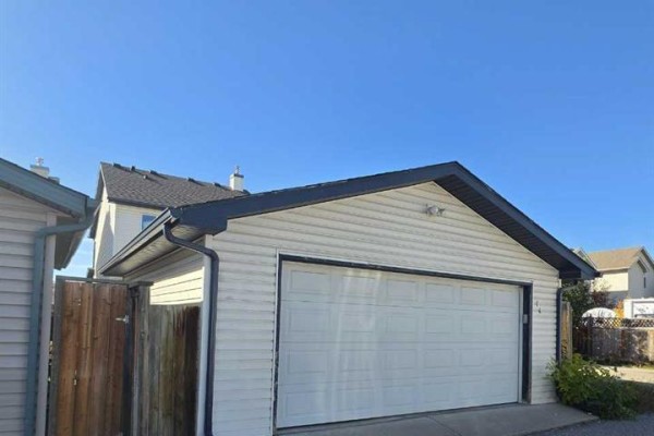 A detached garage with a white overhead door and light beige vinyl siding sits on a gravel driveway. - 14 Bridlewood Manor Sw, Calgary