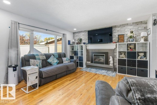 Living room with fireplace, mounted television, large sliding window, and hardwood flooring. - 14 Circlewood Dr, Sherwood Park