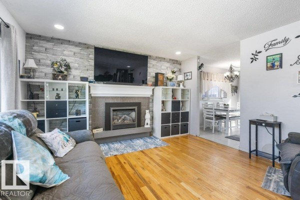 Living room with fireplace and television, connected to a dining area with a chandelier. - 14 Circlewood Dr, Sherwood Park