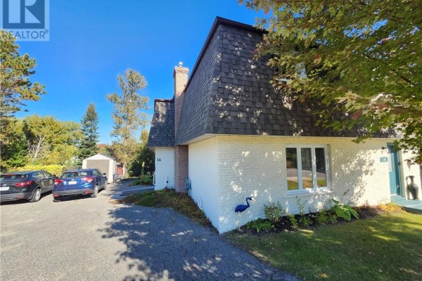 Side view of a white brick house with a dark shingled mansard roof, driveway, and green lawn. - 14 Collins, Copper Cliff