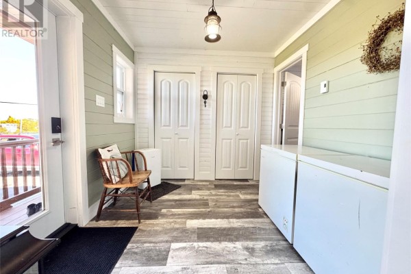 Interior view of an entryway with a wooden chair, chest freezers, and double white doors. - 14 Durrell Street, Twillingate