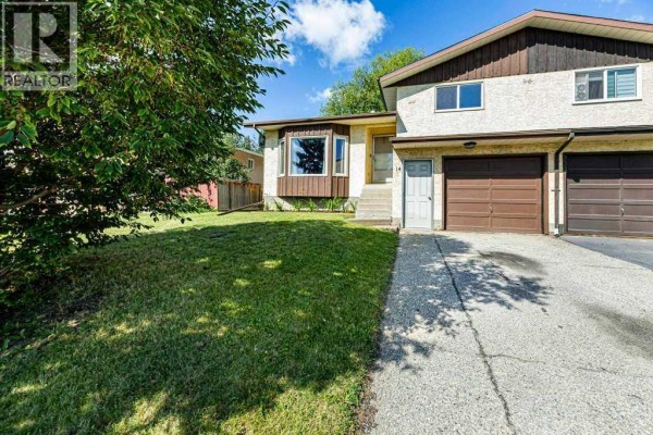 Side exterior view of a light-colored duplex with brown trim and two attached garage doors. - 14 Eagle Road, Lacombe