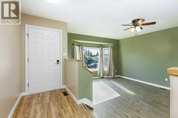 Interior view of the entrance hallway and living room with green walls and wood-look flooring. - 14 Eagle Road, Lacombe