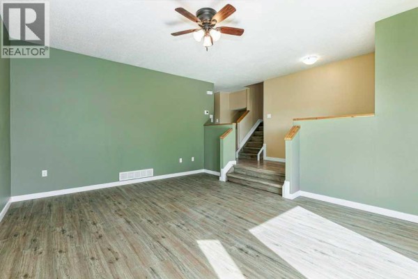 Living room with green and tan walls, wood-look flooring, and a view of the staircase. - 14 Eagle Road, Lacombe