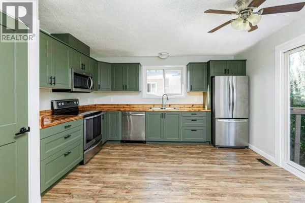 Kitchen with green cabinets, stainless steel appliances, wood countertops, and wood-look flooring. - 14 Eagle Road, Lacombe