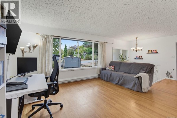 Living room with wood floors, a grey sofa, and a large window overlooking the street. - 14 Eaton Ave, View Royal