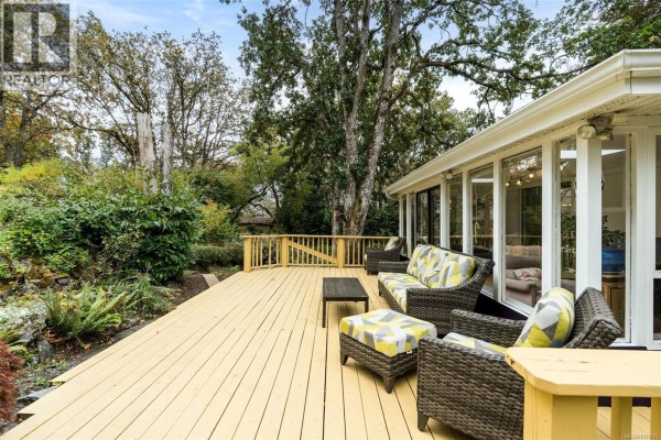 Wooden deck with wicker furniture and a coffee table, overlooking a garden area. - 14 Eaton Ave, View Royal