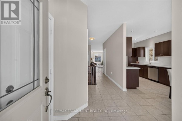 View from the entryway into the home, showing tiled floors and a dark wood kitchen. - 14 Ecker Lane, Hamilton