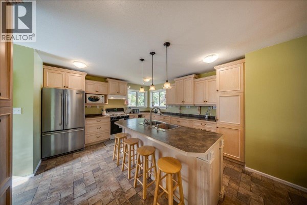 Kitchen island with pendant lights, light wood cabinets, stainless steel appliances, and tiled flooring. - 14 Hillside Drive, Trail
