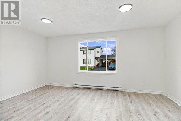 Empty room with light wood laminate flooring, white walls, and a large window with exterior view. - 14 Jubilee Place, Mount Pearl
