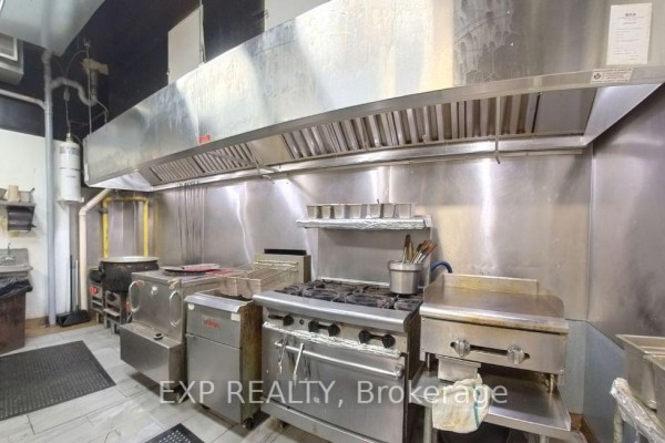 Commercial kitchen with stainless steel equipment including a stove, deep fryers, and ventilation hood. - 14 King Street W, Oshawa