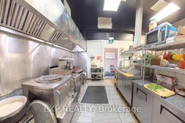 Commercial kitchen with stainless steel counters, shelves, microwave, and various cooking appliances. - 14 King Street W, Oshawa