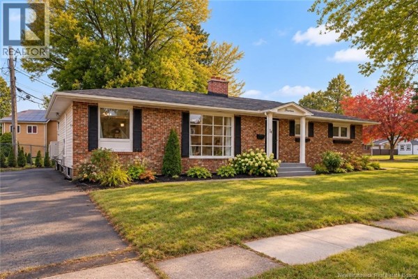 Side view of a red brick bungalow with a paved driveway and surrounding greenery. - 14 Laird, Moncton