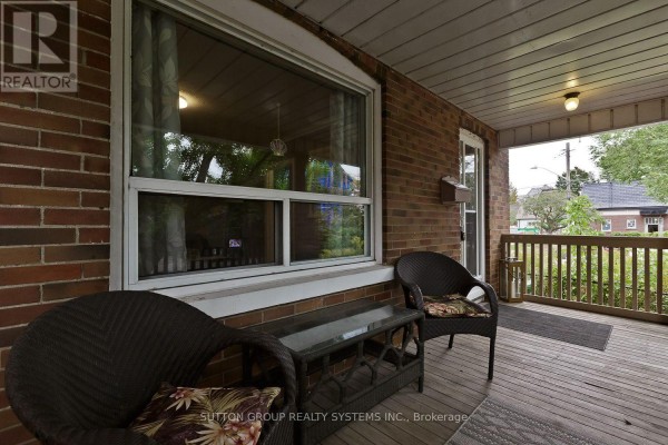 Covered front porch with wicker chairs, a glass-top table, and a brick wall. - 14 Lake Shore Drive, Toronto