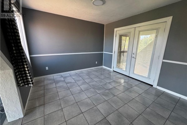 Empty room with grey walls, white trim, and double glass doors to a deck. - 14 Lynne Court, Chapleau