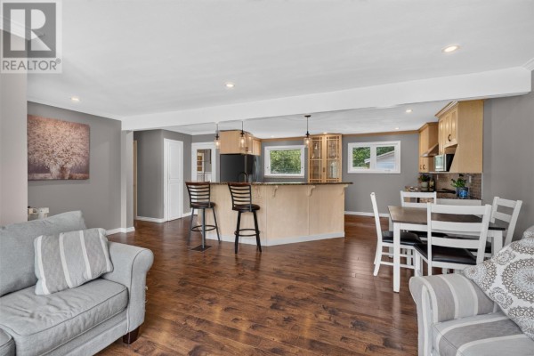Living area adjacent to kitchen and dining room, featuring grey sofas, a wooden dining table, and island stools. - 14 O'regan Road, St  John S