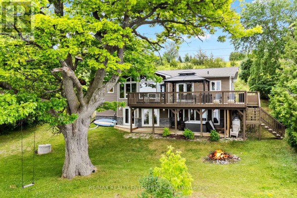 Rear view of a multi-level home featuring a large deck, hot tub, and a campfire. - 14 Parker Drive, Alnwick/haldimand