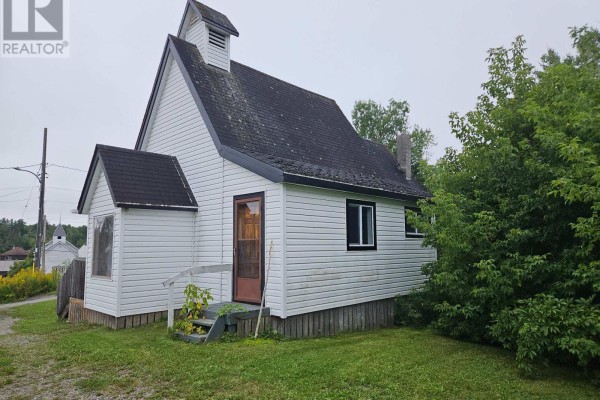 Side view of the white building showing a wooden door and green trees. - 14 Parkwood Lane, Temagami