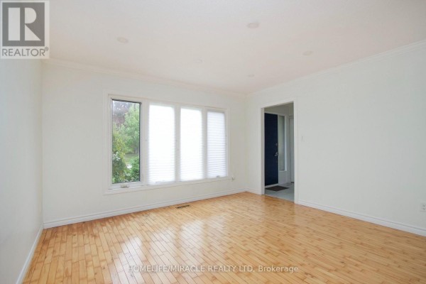 Living room with light wood floors, white walls, and a large window with blinds, showing an exterior view. - 14 Pilkington Crescent N, Whitby