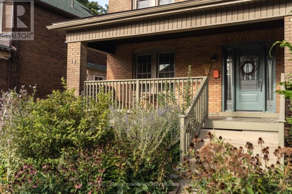 Close-up of the front porch with railing, green front door, and surrounding garden plants. - 14 Prospect Street S, Hamilton