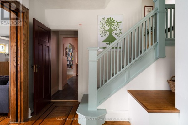 Interior staircase with light blue banister, wood floors, and view into a room with bookshelves. - 14 Prospect Street S, Hamilton