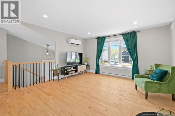 Living room with light wood floors, green armchair, and large window with teal curtains. - 14 Robert Street, Shediac