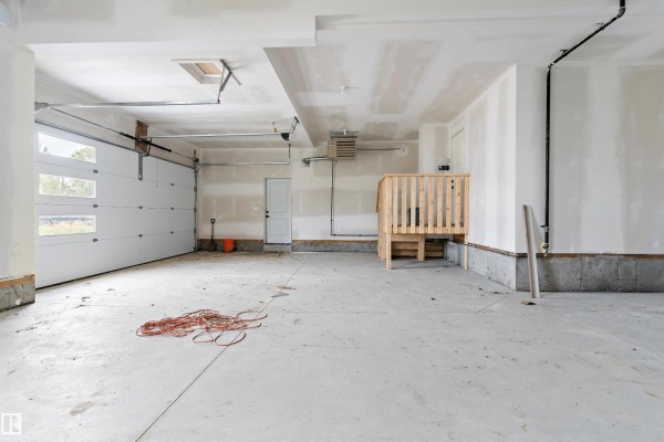 Unfinished garage interior with a white garage door, concrete floor, and wooden stairs. - 14 Southbridge Dr, Calmar