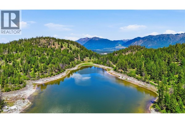 Aerial perspective of a calm lake surrounded by evergreen trees and hills, with mountains beyond. - 14 Sub Lot 3/93 Highway, Cranbrook