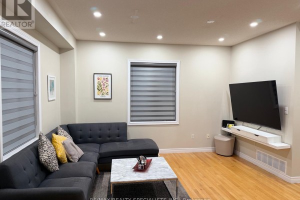 Living room with a sectional sofa, television on wall-mounted shelf, and striped blinds. - 14 Viceroy Crescent, Brampton