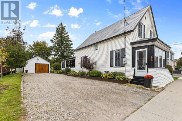 Side exterior view of a white house with a detached garage and gravel driveway. - 14 Victoria Avenue, North Grenville