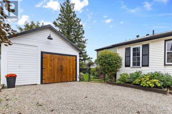 Gravel driveway with a detached garage featuring wooden doors and a white exterior. - 14 Victoria Avenue, North Grenville