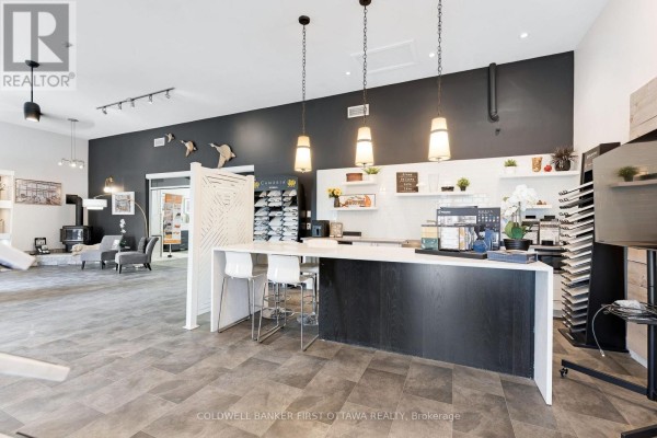 View down a commercial space showing a white counter, display shelves, and a sink area. - 140 Industrial Avenue, Carleton Place