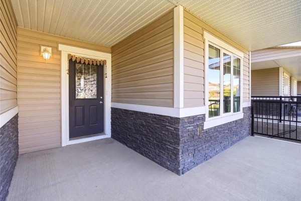 Covered porch entrance with tan siding, grey stone accents, and a dark door. - 140 Park East Drive, Winnipeg