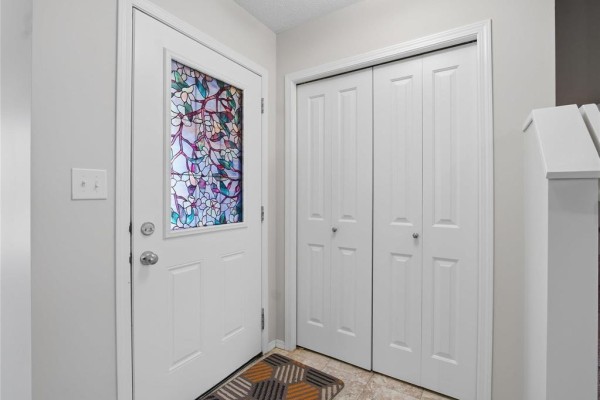 Interior entryway with a white door featuring stained glass and two white bi-fold closet doors. - 140 Park East Drive, Winnipeg
