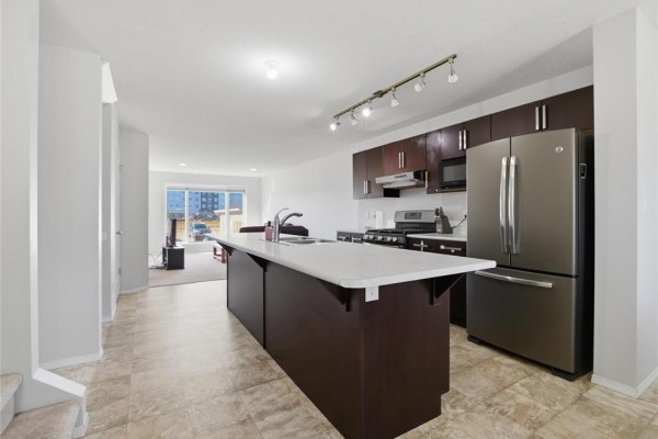 Kitchen with a dark brown island, dark brown cabinets, stainless steel appliances, and beige tile floor. - 140 Park East Drive, Winnipeg