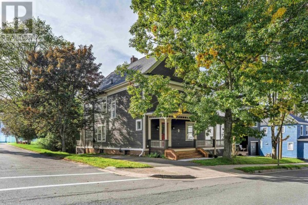 Side view of a dark brown Victorian house with a porch and trees. - 140 Pleasant Street Street, Truro