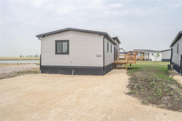 Side view of a modular home with grey siding and black trim, number 140 visible, next to a gravel area. - 140 Prairie Oak Drive, Mitchell