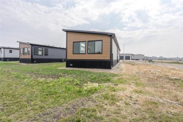 Row of modern modular homes with grey and brown siding under a cloudy sky, grassy field in foreground. - 140 Prairie Oak Drive, Mitchell