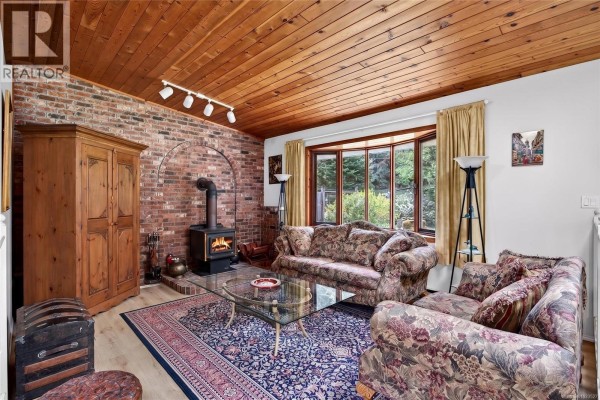 Living room with floral sofas, bay window, wood ceiling, and view to hallway. - 140 Quarry Dr, Salt Spring