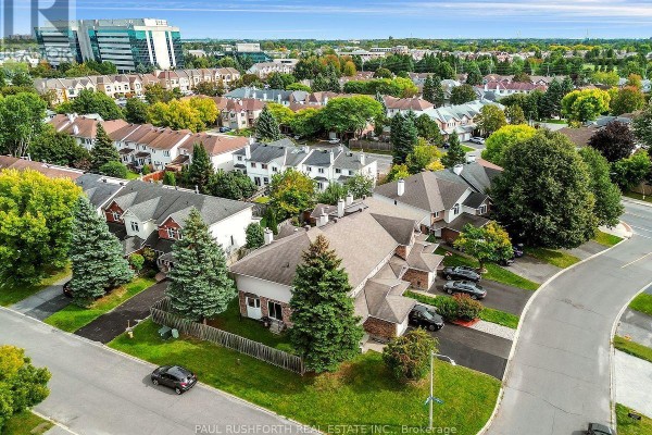 Aerial view of townhouses with surrounding streets, trees, and a distant city skyline. - 140 Thornbury Crescent, Ottawa