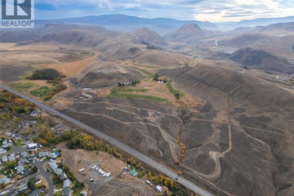 Wide aerial perspective of hilly terrain, residential areas, and a highway in Cache Creek. - 1400 Fehr Way, Cache Creek