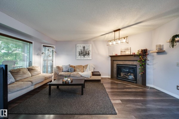 Living room showing beige sectional sofa, dark coffee table, and gas fireplace. - 14006 158a Av Nw, Edmonton