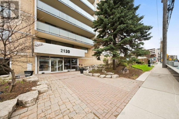 View of the building entrance and walkway from the side, with a sidewalk. - 1401 - 2130 Weston Road, Toronto